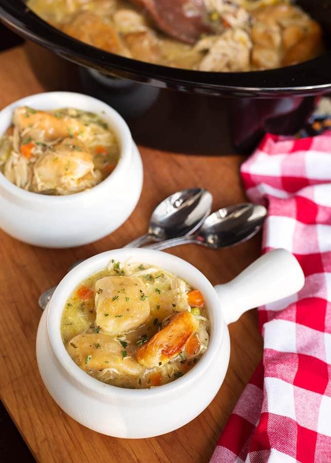 Two white bowls of Chicken and Dumplings in front of a slow cooker