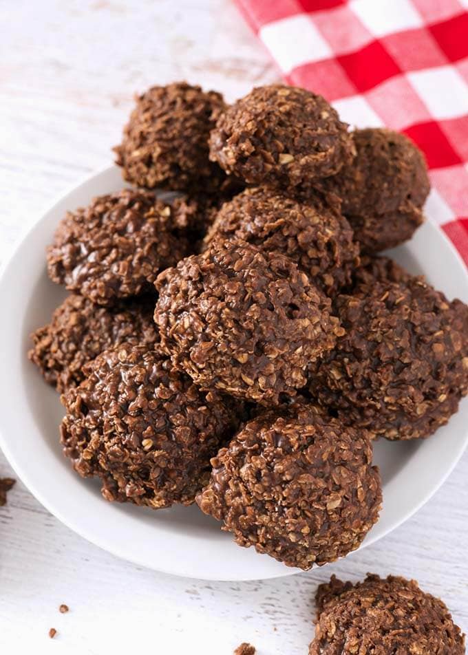 A pile of Chocolate Peanut Butter No Bake Cookies on a white plate next to a red gingham napkin