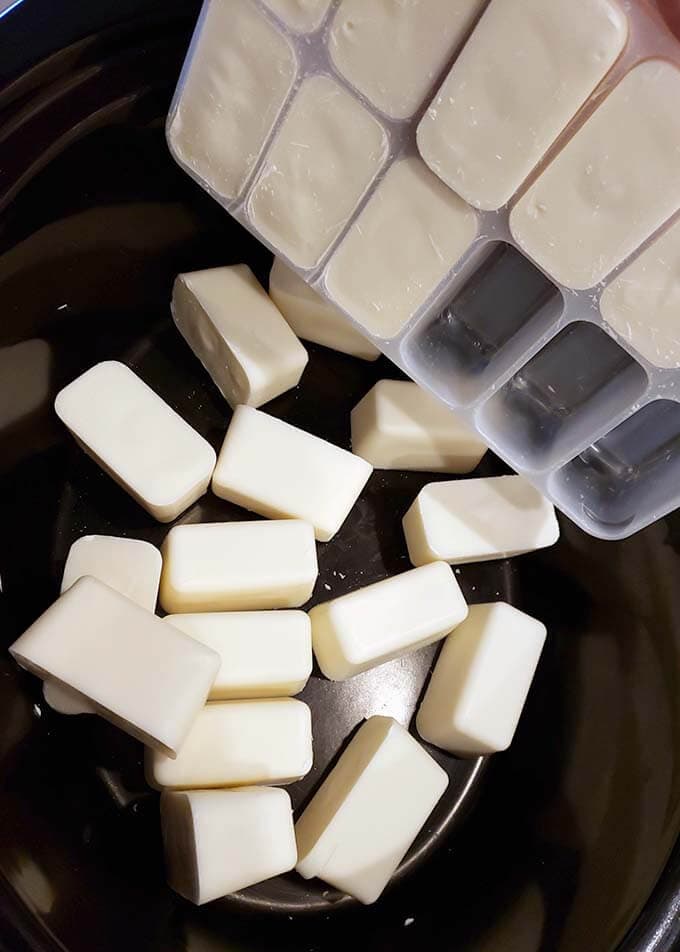 Several white chocolate pieces being dumped from a tray into the slow cooker