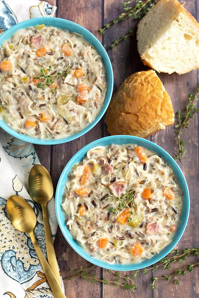 Top view of two blue bowls of Creamy Chicken Wild Rice Soup next to cut bread