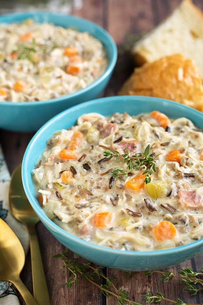 Two blue bowls of Creamy Chicken Wild Rice Soup next to cut bread