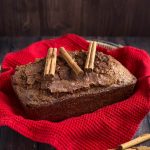 Whole loaf of Nana's Easy Cinnamon Bread topped with three cinnamon sticks all on top of a basket lined with a red napkin