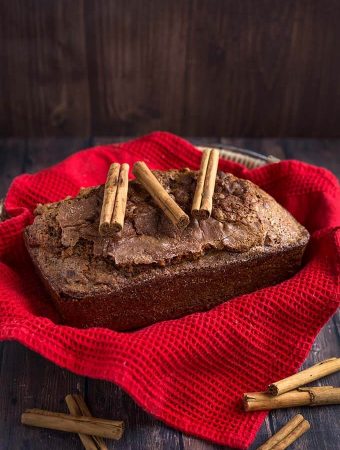 Whole loaf of Nana's Easy Cinnamon Bread topped with three cinnamon sticks all on top of a basket lined with a red napkin