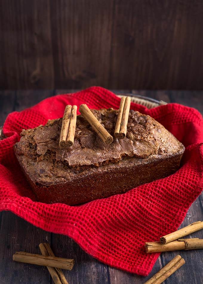 Whole loaf of Nana's Easy Cinnamon Bread topped with three cinnamon sticks all on top of a basket lined with a red napkin