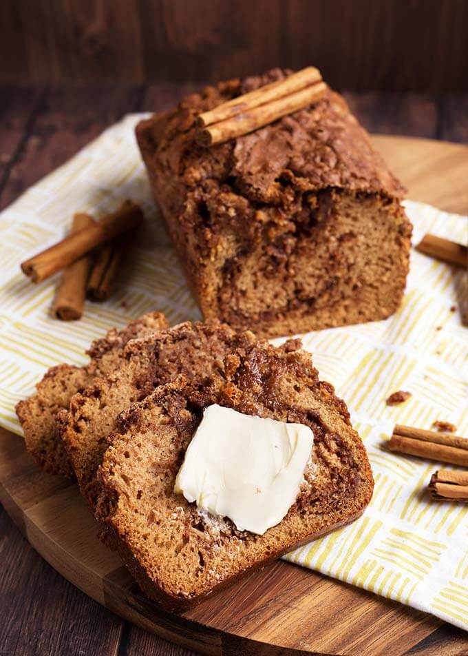 Slices of Nana's Easy Cinnamon Bread with slice of butter in front of loaf and cinnamon sticks