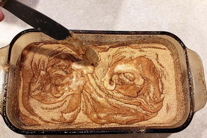 whirling cinnamon and sugar with a knife in a glass pan of unbaked cinnamon bread