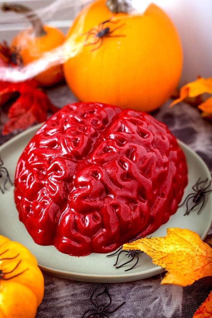 Halloween Jello Brain on a green plate with plastic black spiders in front of a small pumpkin