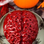 Halloween Jello Brain on a green plate with plastic black spiders in front of a small pumpkin