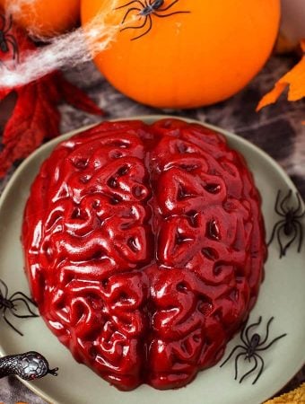 Halloween Jello Brain on a green plate with plastic black spiders in front of a small pumpkin