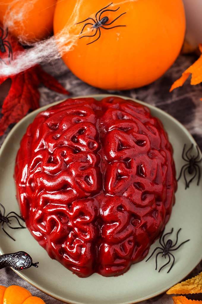 Halloween Jello Brain on a green plate with plastic black spiders in front of a small pumpkin