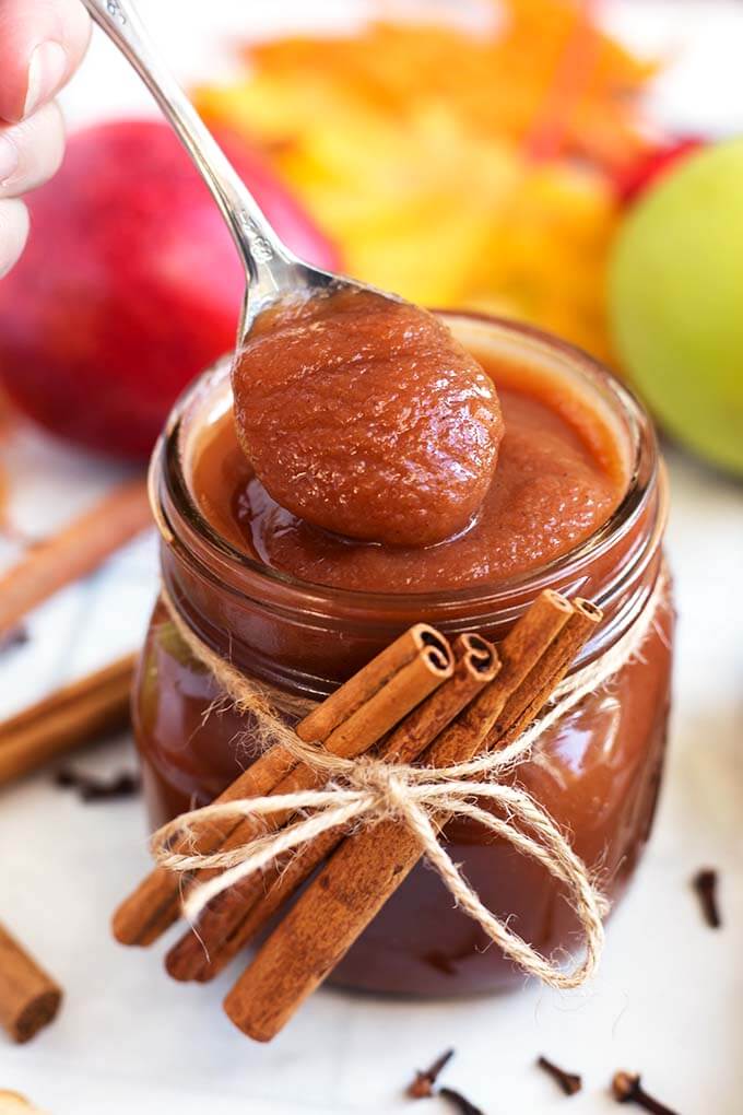 Closeup of a spoonful of Apple Butter from a Small glass jar of Apple Butter with cinnamon sticks tied with twine