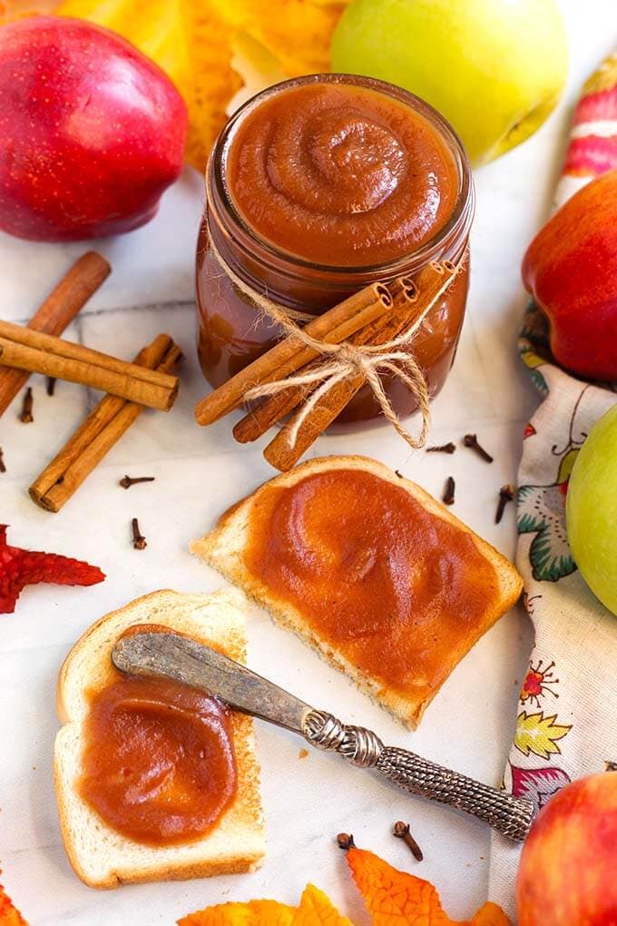 Small jar of Apple Butter tied with cinnamon sticks behind toast with apple butter spread on it