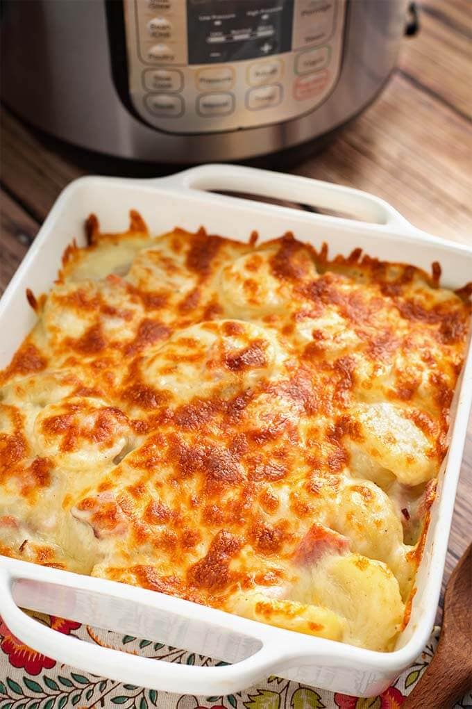 Scalloped Potatoes in a square white baking dish in front of a pressure cooker