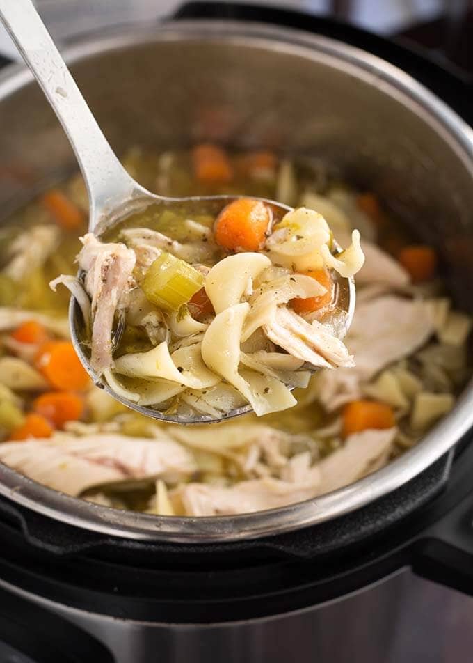 Closeup of a ladle full of Chicken Noodle Soup over a pressure cooker with the soup in it