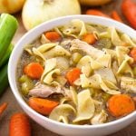 Chicken Noodle Soup in a white bowl surrounded by vegetables
