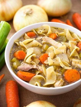 Chicken Noodle Soup in a white bowl surrounded by vegetables
