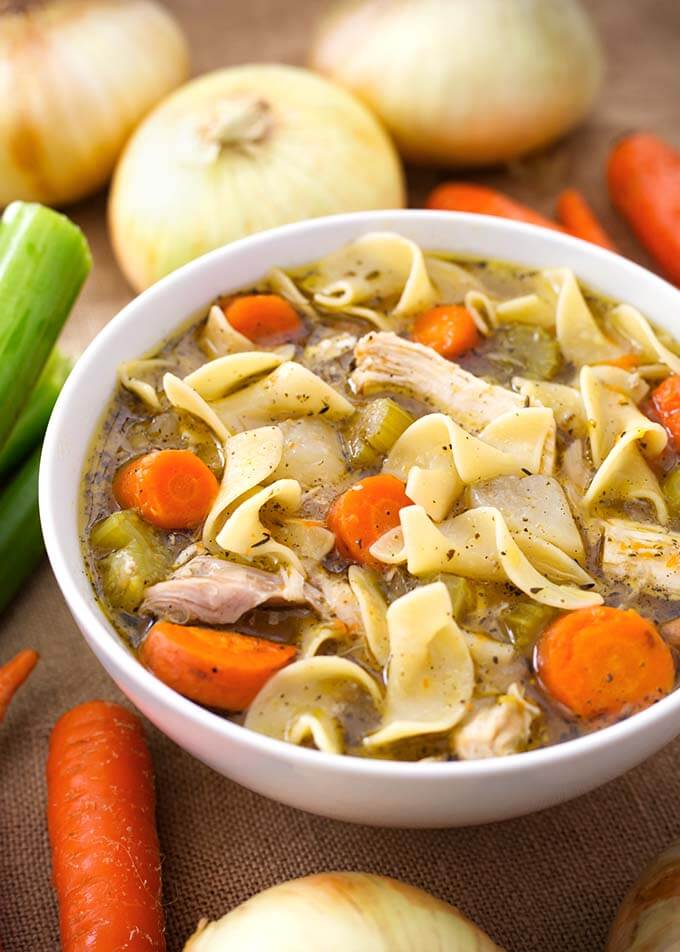 Chicken Noodle Soup in a white bowl surrounded by vegetables