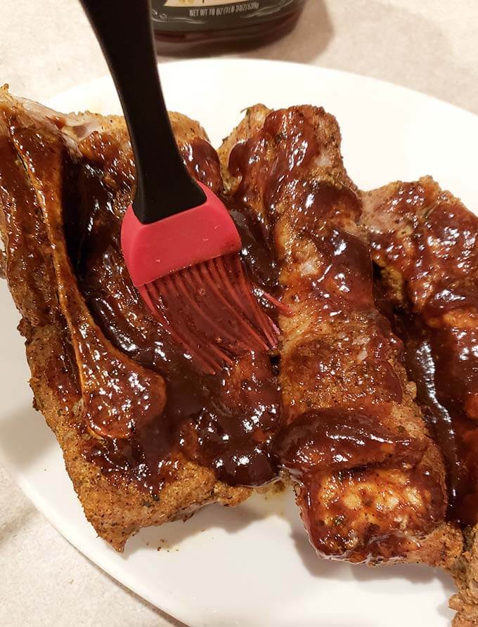red sauce brush slathering barbecue sauce onto Country Style Ribs on a white plate