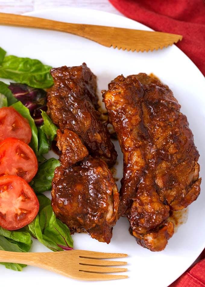 Country Style Ribs on a white plate with vegetables and a wooden fork and knife