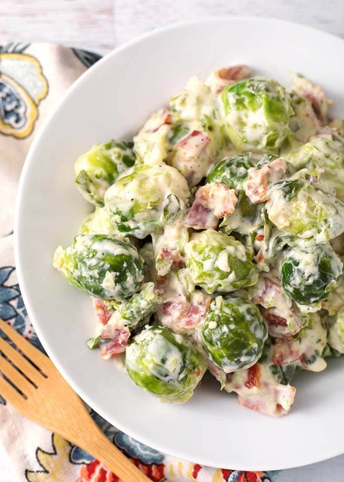 Creamy Bacon Brussels Sprouts on a white plate next to a wooden fork