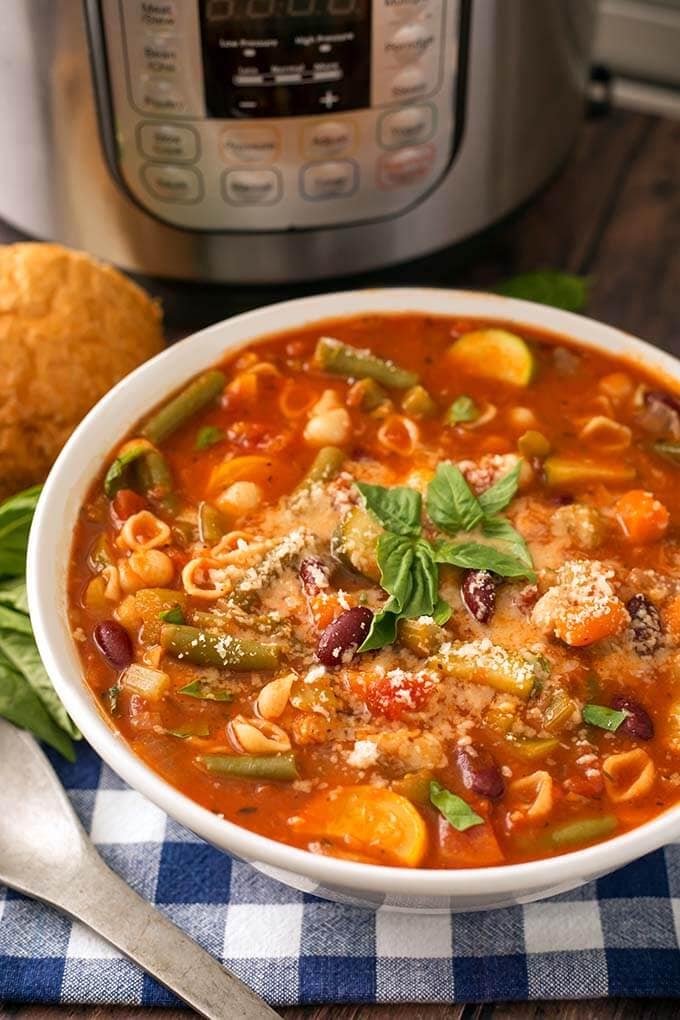Minestrone Soup in a white bowl in front of a pressure cooker