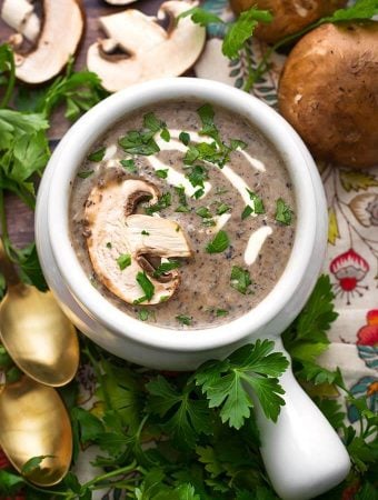 Top view of Mushroom Soup in a white handled bowl topped with a fresh mushroom slice and parsley