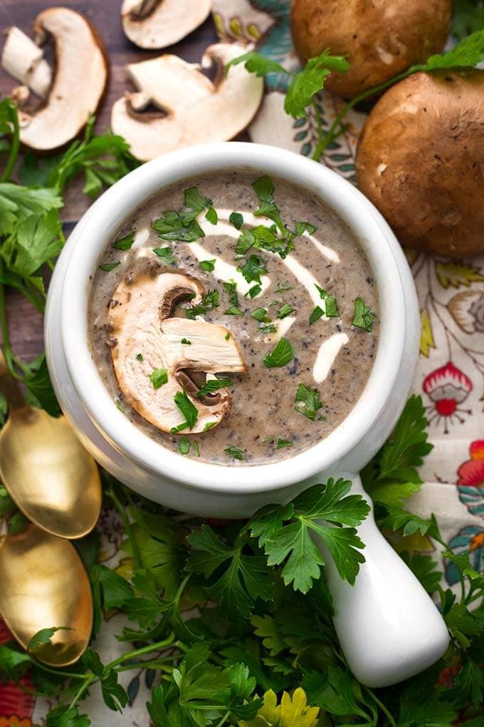 Top view of Mushroom Soup in a white handled bowl topped with a fresh mushroom slice and parsley