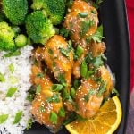 Orange Chicken Legs with rice, broccoli, and an orange slice on a square black plate