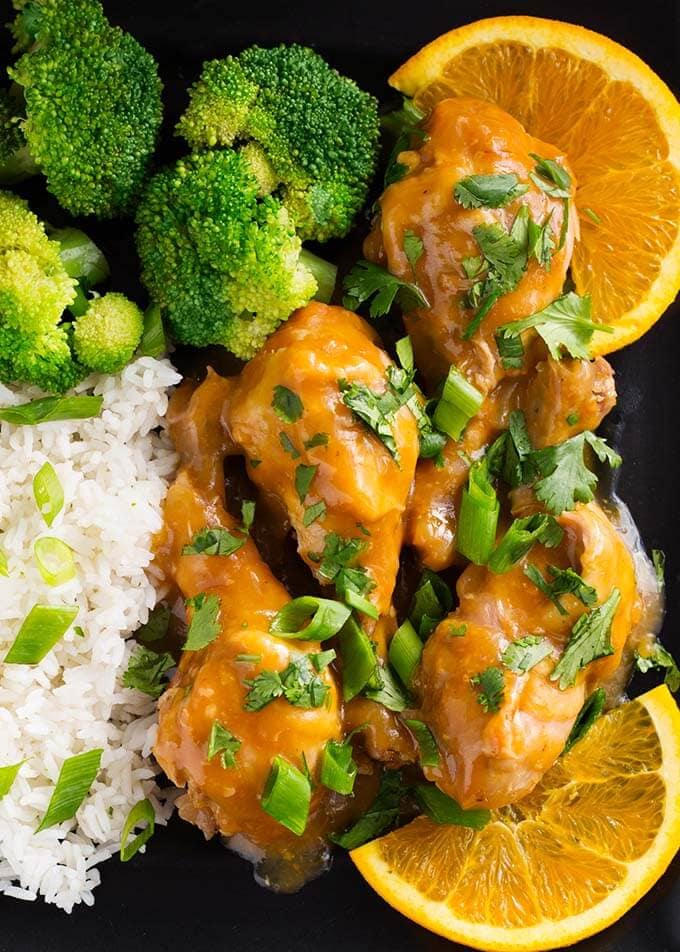 Closeup of Orange Chicken Legs with rice, broccoli, and an orange slice on a square black plate