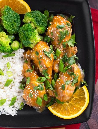 Orange Chicken Legs with rice, broccoli, and an orange slice on a square black plate