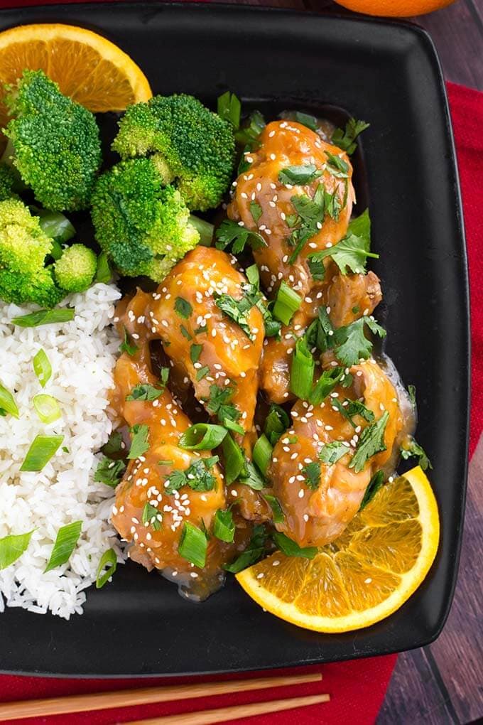 Orange Chicken Legs with rice, broccoli, and an orange slice on a square black plate