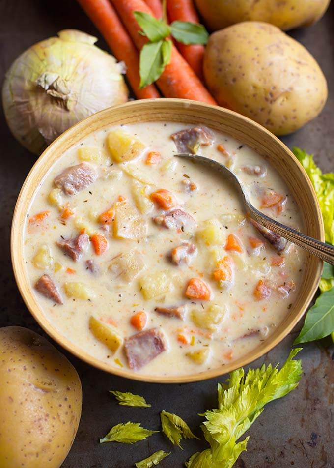 Potato Ham Soup and silver spoon in a beige bowl surrounded by vegetables