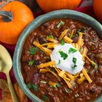 Pumpkin Chili topped with shredded cheese and sour cream in a turquoise bowl