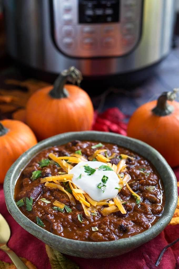 Pumpkin Chili topped with shredded cheese and sour cream in a turquoise bowl in front of a pressure cooker