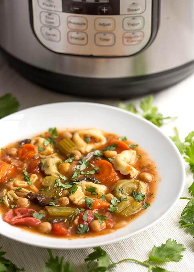 Vegetable Tortellini Soup in a white bowl in front of a pressure cooker