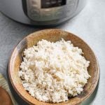 White Rice in a brown stoneware bowl in front of a pressure cooker