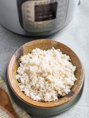 White Rice in a brown stoneware bowl in front of a pressure cooker