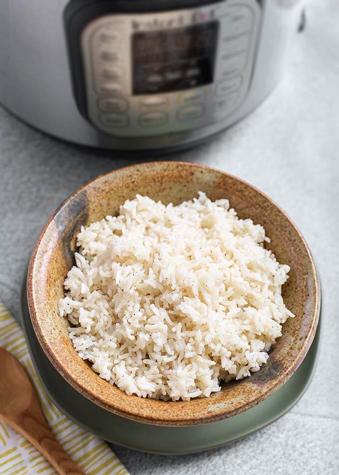 White Rice in a brown stoneware bowl in front of a pressure cooker