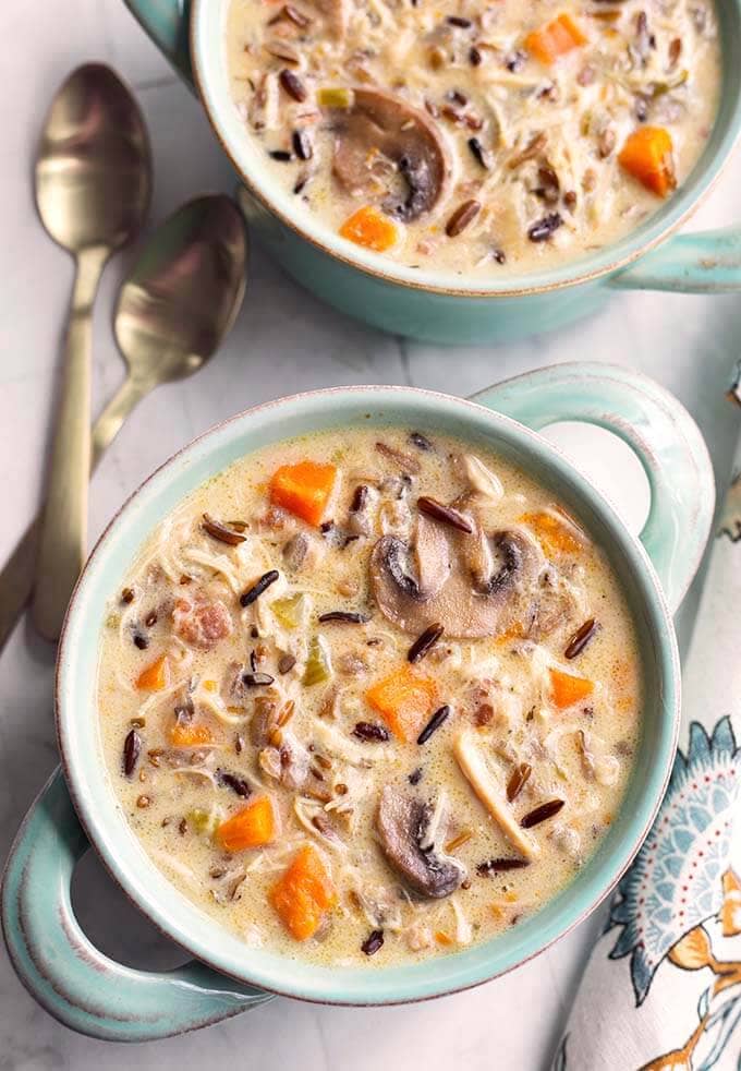 Two blue bowls with handles of Wild Rice Soup with Chicken next to two spoons