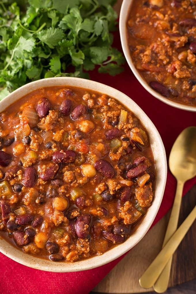 Two beige bowls full of Turkey Chili next to two gold spoons