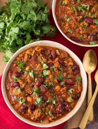 Two beige bowls full of Turkey Chili next to two gold spoons