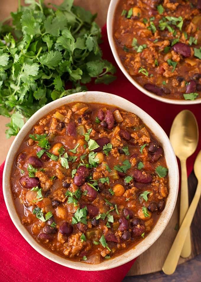 Two beige bowls full of Turkey Chili next to two gold spoons