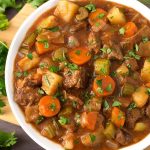 Classic Beef Stew in a white bowl on a wooden board next to fresh parsley