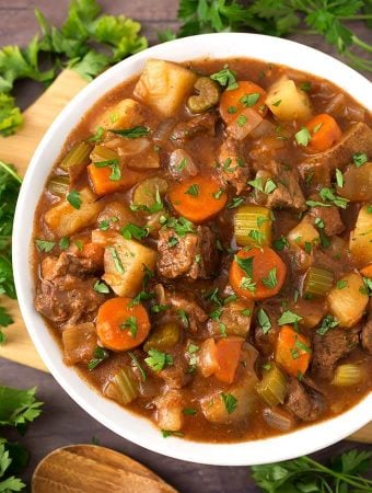 Classic Beef Stew in a white bowl on a wooden board next to fresh parsley