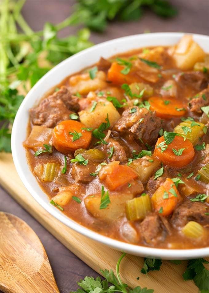 Classic Beef Stew in a white bowl on a wooden board next to fresh parsley