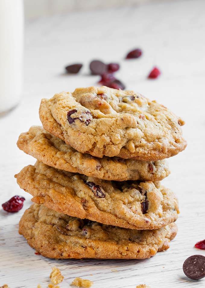 Four Cranberry Dark Chocolate Cookies stacked on a white wood background