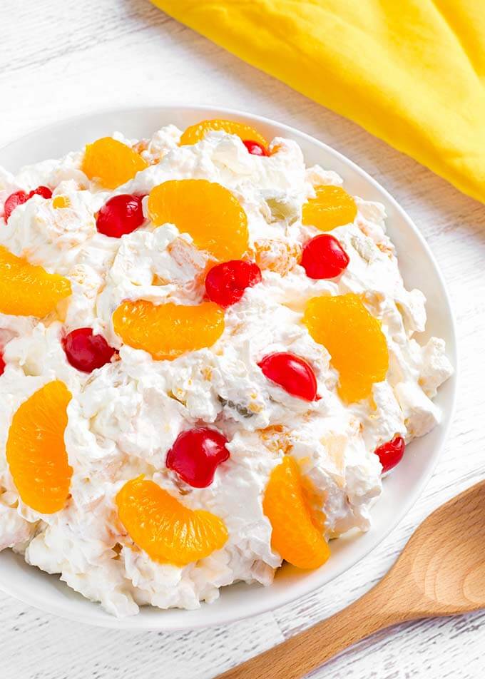 Creamy Cheesecake Fruit Salad in a white bowl on a white wood background