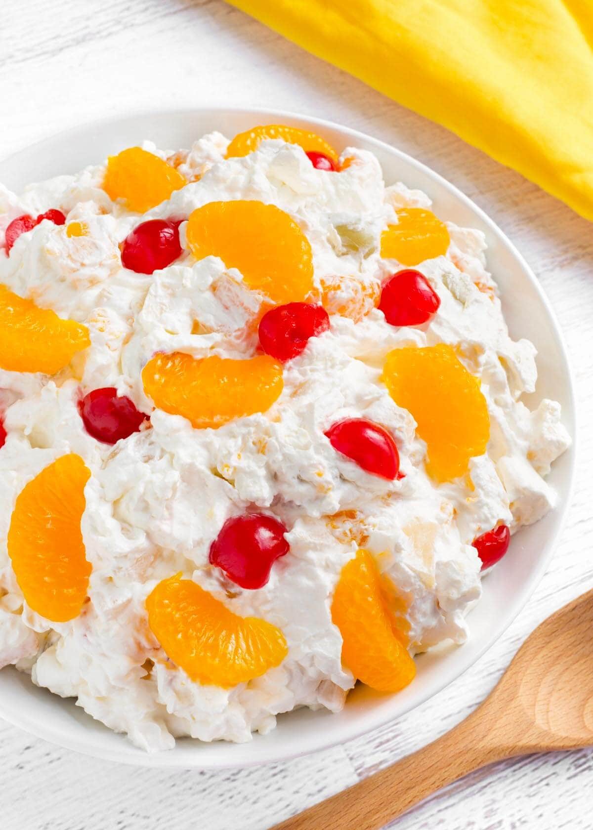 Creamy Fruit Salad in white bowl, yellow linen, wood spoon