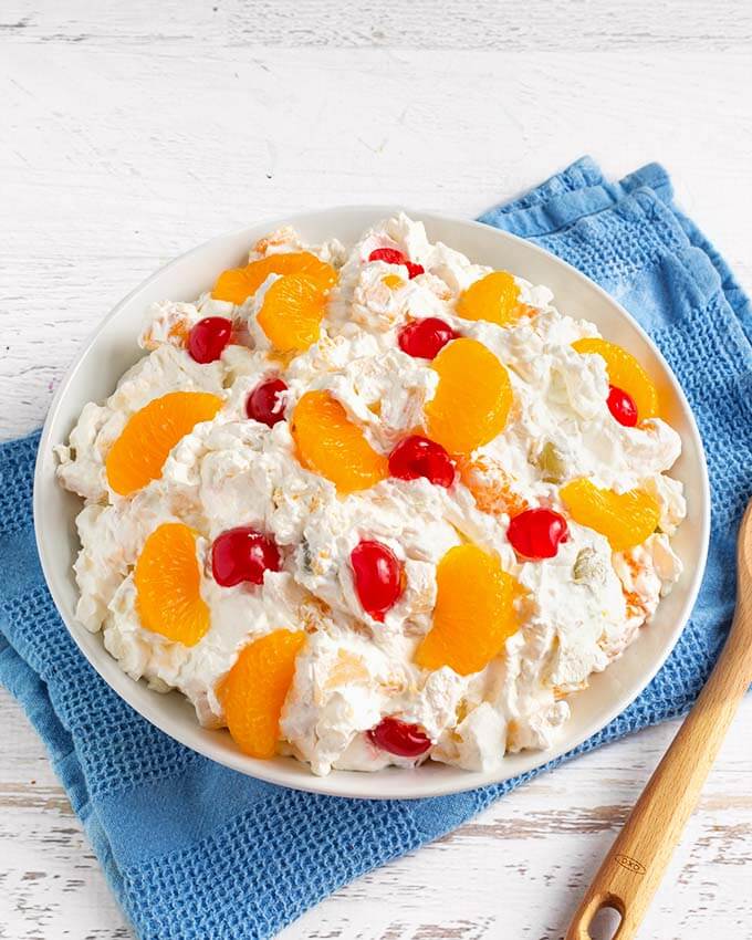 Top view of Creamy Cheesecake Fruit Salad in a white bowl on top of a blue napkin