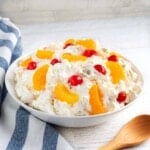 Creamy Fruit Salad in a white bowl with wood spoon and striped napkin.